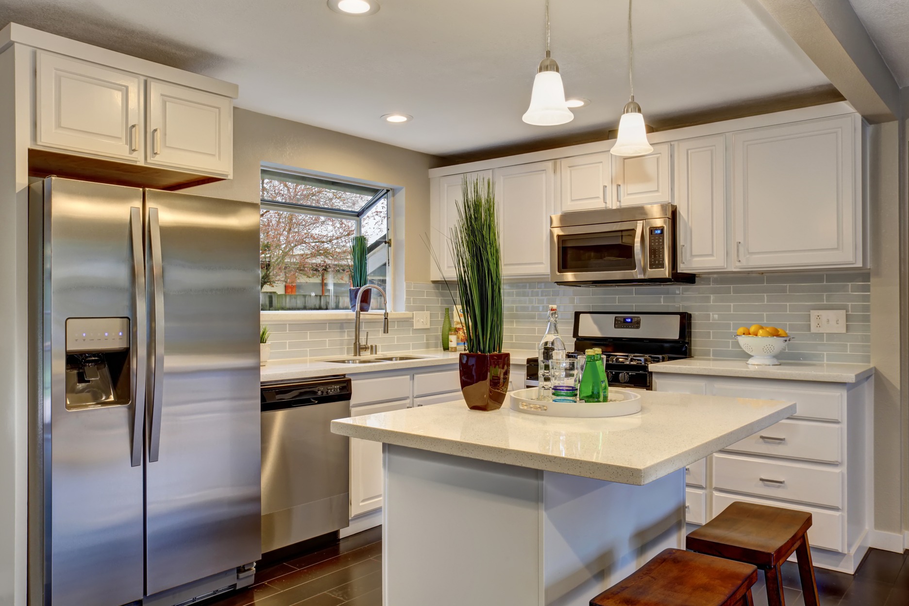 Modern kitchen featuring stainless steel appliances, white cabinetry, and a large island with seating. Natural light illuminates the space through a window.